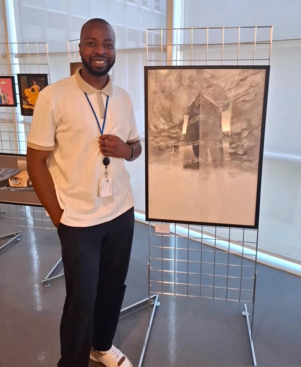 Andy, artiste dessinateur, aux côtés de son dessin architectural encadré